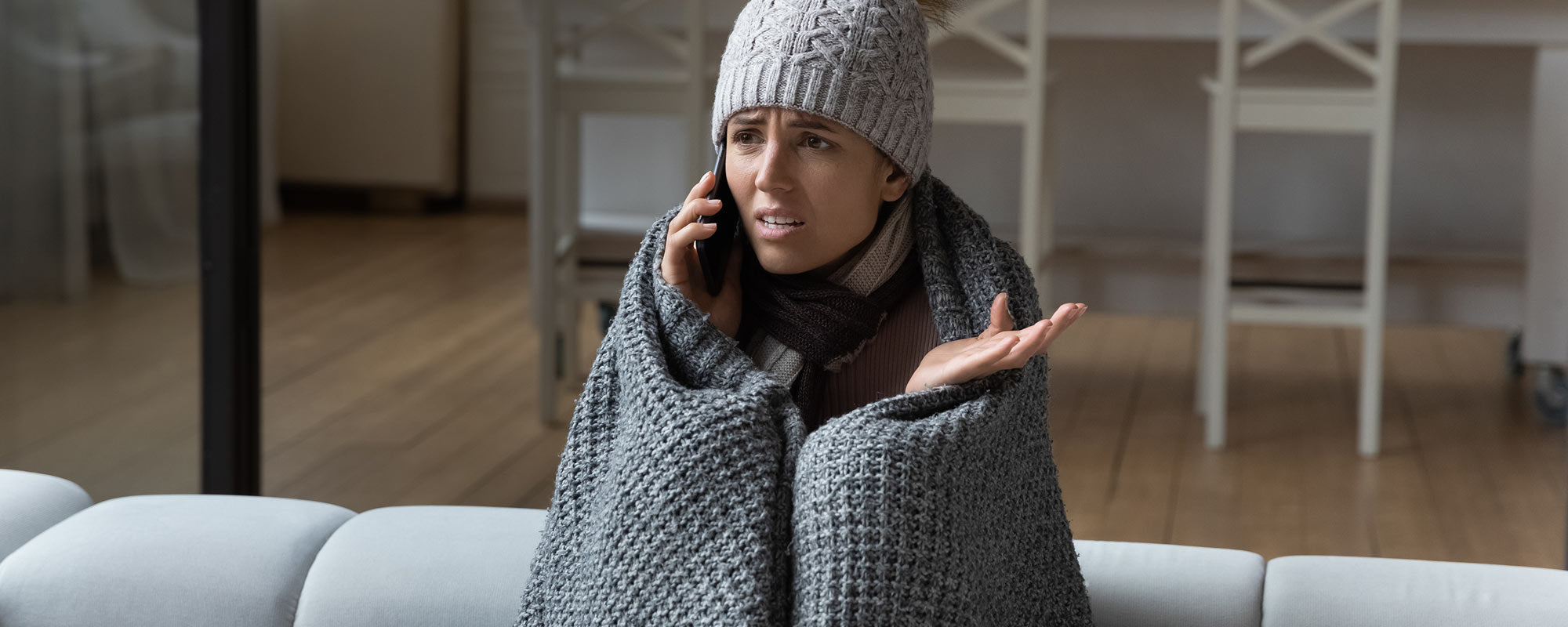 woman sitting on couch covered in blanket and wearing winter hat