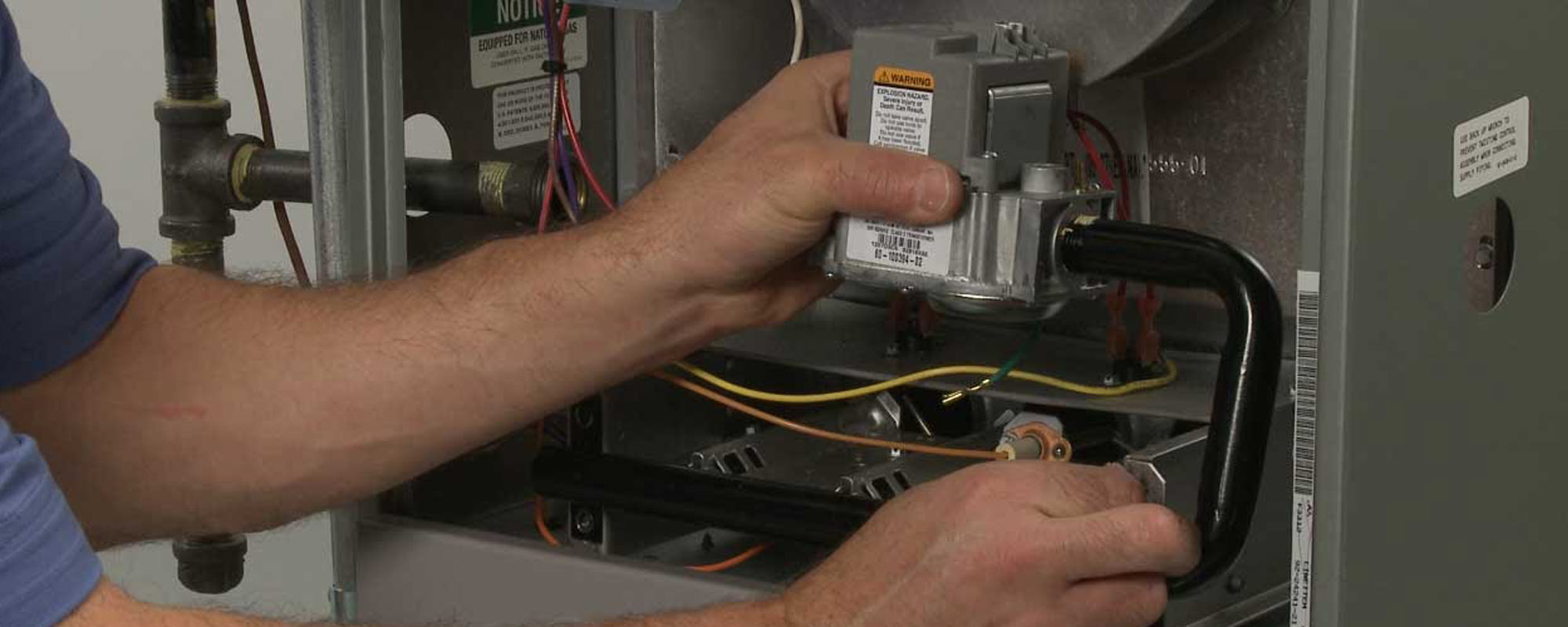 man looking at inside of furnace holding onto gas valve