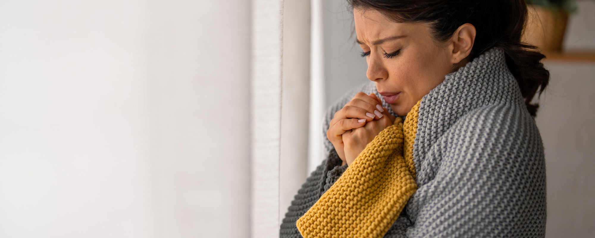 woman trying to get warm cupping hands with blanket because furnace wont turn on