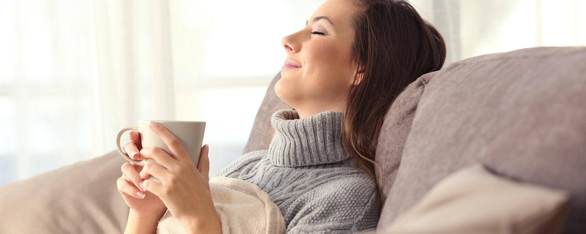 young woman sitting on couch with cup in hand enjoying heating system