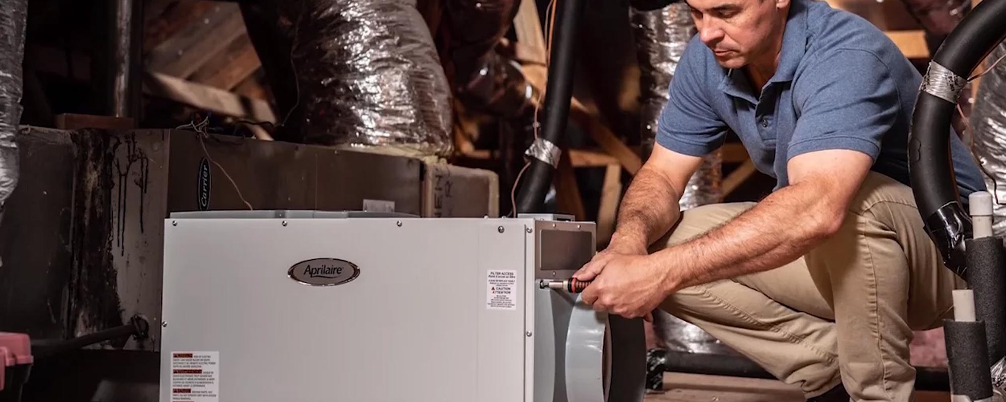 man installing whole house dehumidifier in attic of home