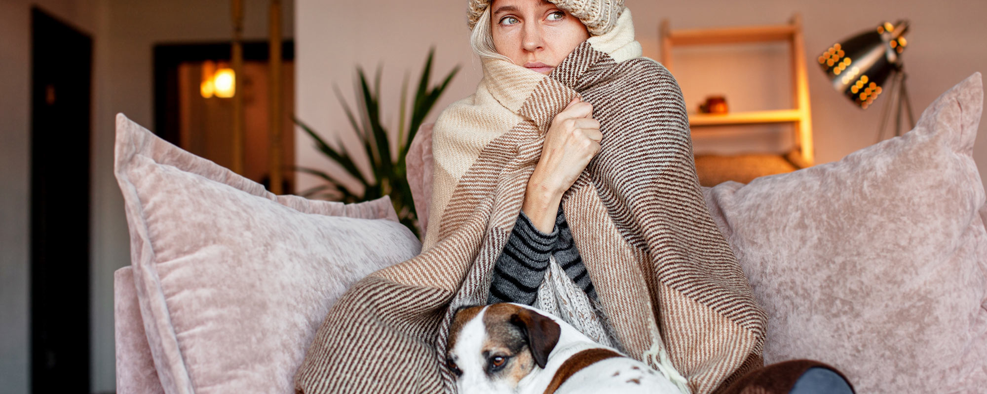 woman sitting on couch with dog covered in blanket because heat pump is blowing cold air