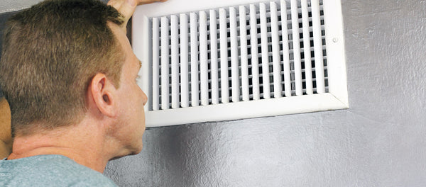man inspecting home vent for cause of musty smell from his air conditioner
