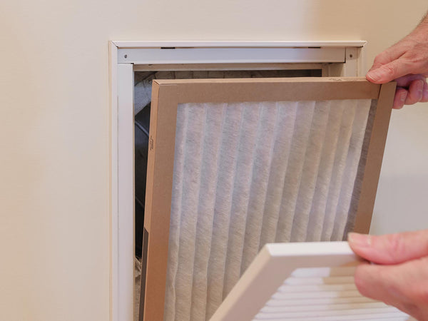 man changing dirty air conditioner air filter from return vent in wall of home