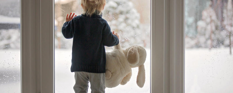 child looking outside of window in home holding stuffed bunny